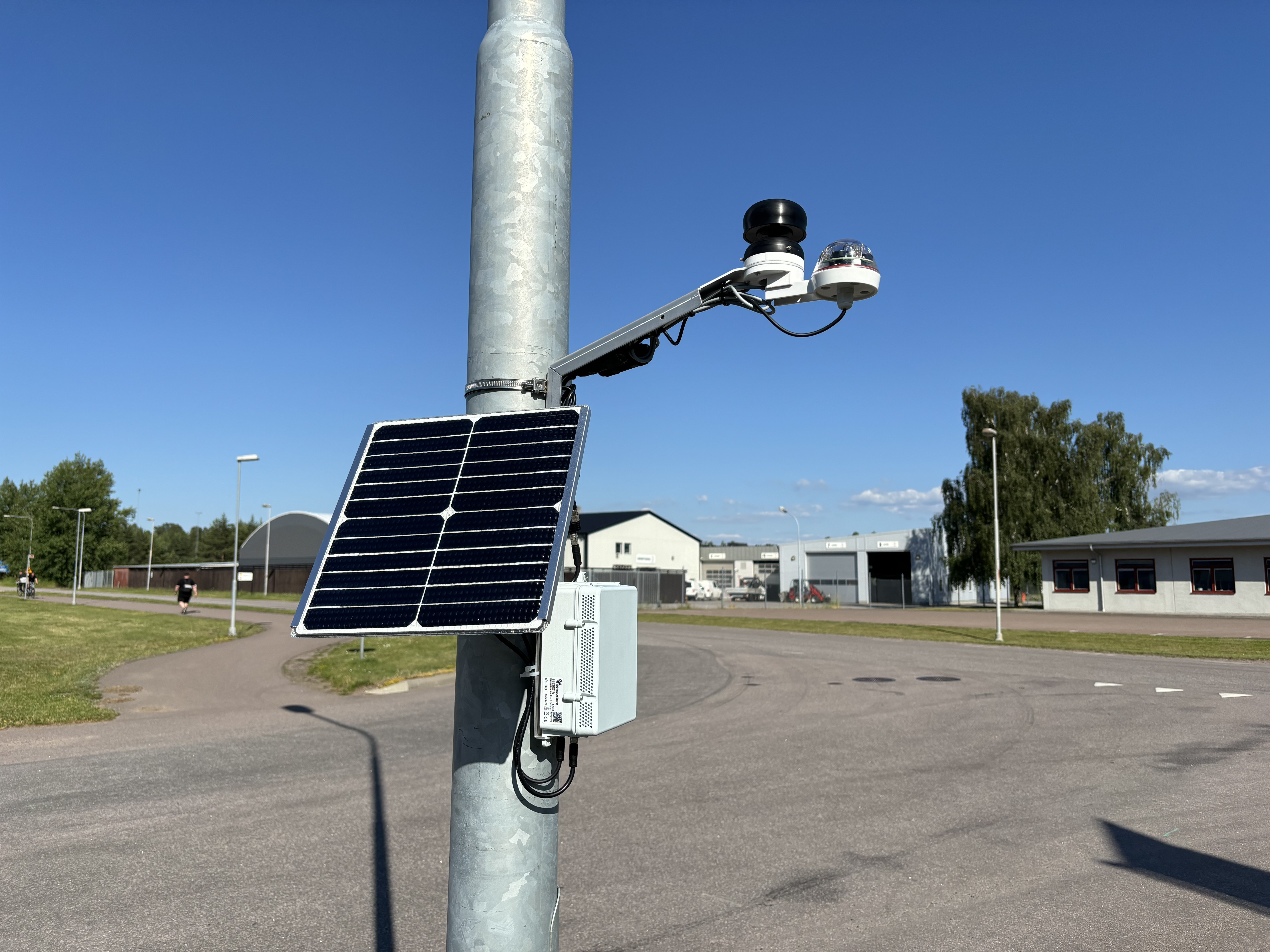 Sensorbee Air Pro 2 napelemes ipari IoT levegőminőség-monitorozó állomás oszlopra szerelve, külső gáz- és szállópor-szenzorokkal egy ipari park területén.