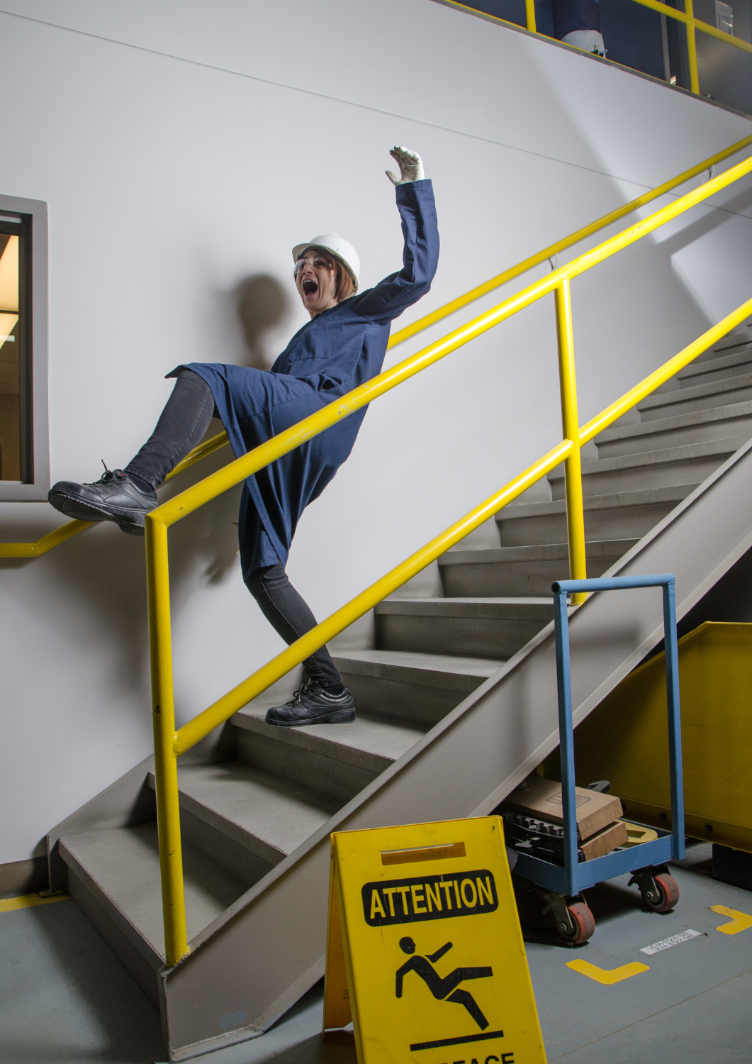Munkabaleset illusztráció: lépcsőn eleső dolgozó egy autógyárban – a Qlight SMP50 hangjelzővel megelőzhető kockázat.